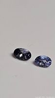 Two oval cut natural tanzanite gemstones displayed on a neutral background, showing their colors and clarity.