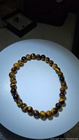 Photo of round polished tiger's eye beads strung on an elastic cord to make a bracelet, showing the golden brown and dark tiger stripes characteristic of tiger's eye gemstone.