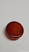 Top-down view of the round orange carnelian cabochon showing its smooth, polished surface and deep orange color.