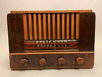 Front view showing wooden cabinet, vertical grille, frequency scale with AM and shortwave bands, and four wooden knobs with age wear.
