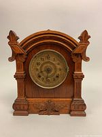 Front view of the wooden Gothic Revival pendulum wall clock showing carved details and brass dial with Arabic numerals.