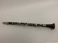 Full length photo of the clarinet showing the dark wood body and silver-colored metal keys against a neutral background.