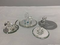 Group photo showing all four Swarovski crystal figurines on beveled mirror display bases including swan with flowers and dog with metallic tail.
