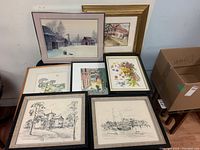 Overview of six framed wall hangings and one serving tray with various scenes and floral art, displayed on a table against a wall.