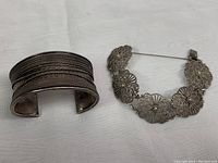 Both silver bracelets side by side; wide cuff bangle on left, filigree bracelet with safety chain on right