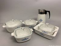 Overall group of four covered Corning Ware baking dishes with blue cornflower design and matching white coffee pot percolator.