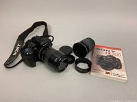 Sony DSLR-a300 camera with Tamron lens, additional lenses, lens hood, caps and Sony DSLR a200 manual booklet laid out on a white background.