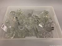 Top-down view of all candlestick holders in a clear plastic bin showing variety of shapes and styles.