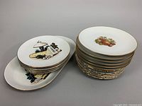 Stack view of plates and oval serving platter, showing gold trim and artwork.