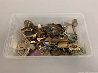 Full view of assorted vintage miniature collectibles in plastic bin showing a mix of gold-tone, brass, pewter, and enamel items.