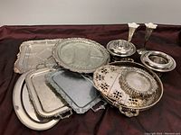 Various silver plated trays and round platters with different decorative edges and patterns.