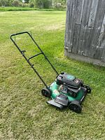 Full view of the green and black push lawn mower on grass, showing handle, wheels, and cutter deck.
