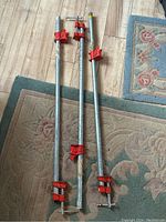 Three 36-inch Bench Mark metal bar clamps with red clamp mechanisms pictured on floor mats, showing overall length and condition.