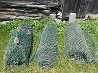 Three rolled up chain link fence sections showing green coating and signs of wear including dirt and bent fencing.