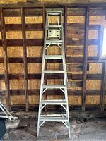 Full view of an 8 foot aluminum step ladder standing upright in a wooden frame space showing its full length and step structure.