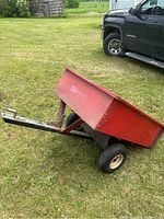 Side front view of entire trailer angled, showing red bed, front hitch, two wheels and frame.