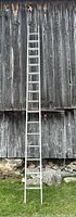 Full view of the aluminum extension ladder placed against a barn wall, showing its length and condition.