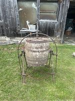 Full view of the oak butter churn with metal frame and crank displayed outside against an old building.