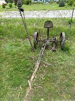 Side view of the entire antique sickle bar side mower showing its structure, wooden tongue beam, and iron wheels.