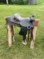Side angle showing the full western saddle with detailed floral tooling on leather skirts and fenders, attached stirrups, and the saddle horn in black leather.