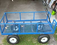Full view of the garden cart from above showing the blue steel mesh construction, handle, and large tires.