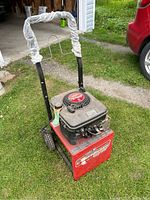 Oblique front-left angled view of generator on grass, showing frame, wheels, and wrapped handle
