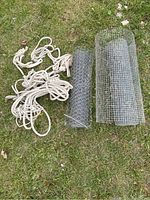 Overview of rolls of chicken wire and coiled ropes laid on grass.