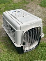 Pet carrier placed outdoors on grass, showing side and front with metal door closed.