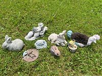 Array of garden figurines on grass, including bunnies, birds, a frog, a turtle, and a decorative sundial.