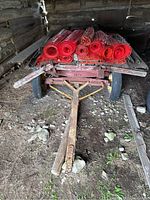 Front view of hay wagon with red painted wooden deck, flat tire, and several rolls of red mesh netting on top.