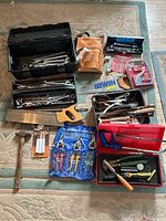 Overview photo of entire tool lot showing wrenches, saw, snips, staple tool, tool pouch, packs of blades, and other hand tools arranged on carpet.