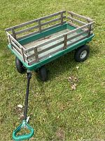 Front and side view of the green wagon showing the wooden slat sides, handle, and tires on grass