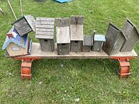 Front view of seven handmade wooden birdhouses on a wooden workbench base on grass.