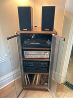 Full view of oak cabinet with glass doors open showing turntable top, silver receiver, black cassette deck, black CD player, vinyl records below and speakers on top