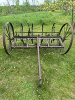 Front view of the antique tractor harrow with metal frame and large spoked wheels, showing width and overall structure.