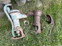 Two vintage hand-operated well pumps on grass showing condition and detached parts