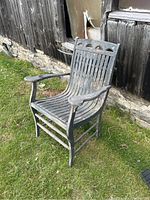 Wooden porch chair outdoors showing front and side view with weathered paint and dirt on grass.
