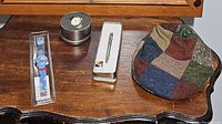 Photo shows Disney Aladdin watch, American Red Cross watch in tin, Disney ballpoint pen in display box, and multicolor patchwork tweed flat cap on wooden table.