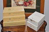 Five boxes of taper and votive candles placed on a wooden table. Three beige boxes of taper candles and two white boxes of votive candles.