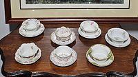 Seven china ramekin and saucer sets displayed on a wooden table, showing various floral patterns and designs.