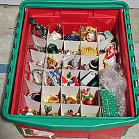 Large red plastic container with green lid filled with cardboard dividers holding assorted vintage glass Christmas ornaments in various shapes and colors.