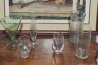 Full set of six glass vases arranged on a wooden surface under framed artwork for scale and context.