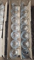 Rows of clear glass votive holders packed in cardboard trays viewed from the top, showing quantity and arrangement.