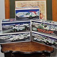 Four Hess toy vehicle collectible sets in their original boxes displayed on a wooden table, including rescue truck and race car sets.