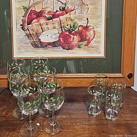 Full set of 6 wine glasses and 4 old fashioned glasses displayed on wood surface with framed apple painting in background.