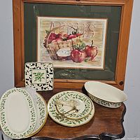 Two oval platters leaning against framed print, round plates with handle and square dish in front, oval casserole on right