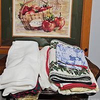 Stack of holiday linens including towels, place mats, and fabric pieces folded on a wooden table.