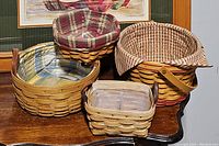 Four Longaberger handmade baskets arranged on a table showing shape, handles, and plaid fabric linings.