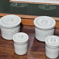 Four ceramic crocks in a set with lids, white glazed, showing woven basket texture.