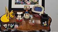 Full view of all items including picture frames, figures, pencil holder, book end, and pins arranged on wooden table with Disney artwork backdrop.